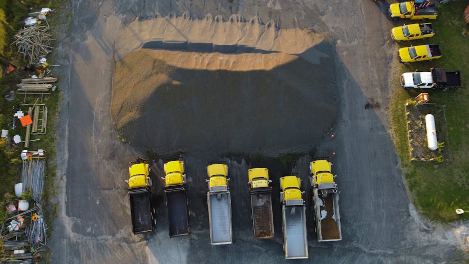 Drone shot of yellow trucks aligned by a gravel heap in New Bern, NC, showcasing industrial work.