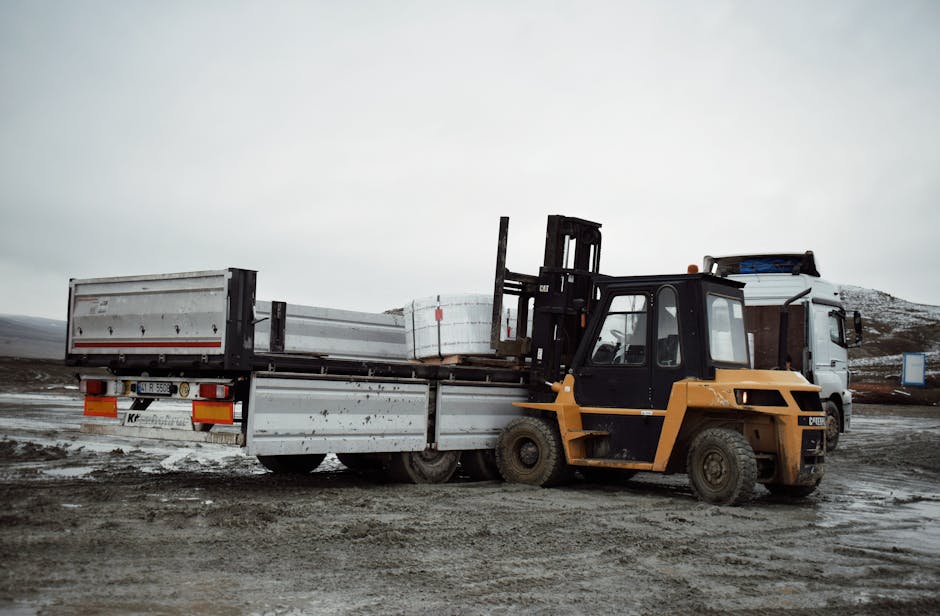 Forklift loading materials onto a truck in an industrial landscape.